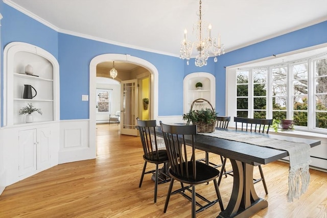 dining area with built in shelves, crown molding, light hardwood / wood-style flooring, and an inviting chandelier