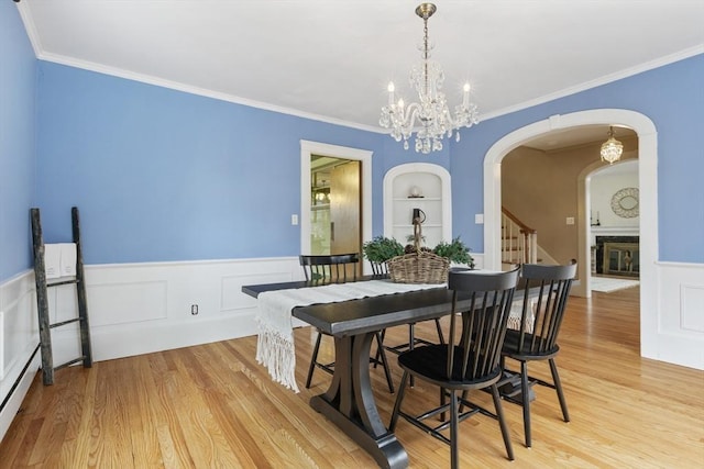 dining room with built in features, an inviting chandelier, ornamental molding, and light hardwood / wood-style flooring