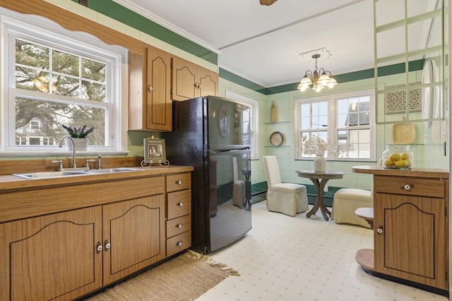 kitchen featuring pendant lighting, an inviting chandelier, black refrigerator, crown molding, and sink