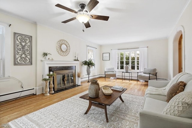 living room with baseboard heating, a premium fireplace, ceiling fan, and hardwood / wood-style flooring