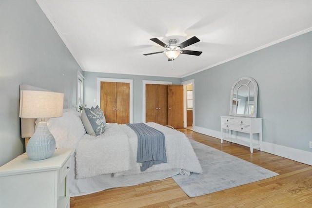 bedroom with hardwood / wood-style floors, ceiling fan, ornamental molding, and multiple closets