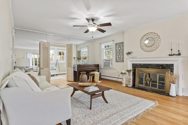 living room featuring ceiling fan, baseboard heating, a high end fireplace, hardwood / wood-style flooring, and ornamental molding