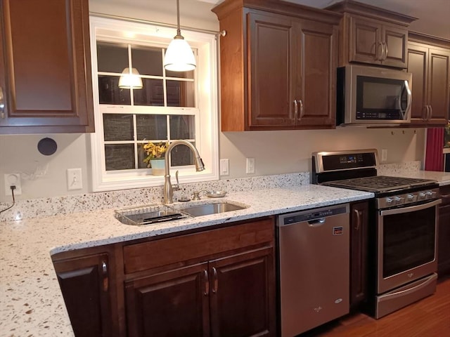 kitchen with appliances with stainless steel finishes, pendant lighting, a sink, and light stone countertops