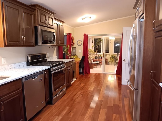 kitchen featuring dark brown cabinetry, lofted ceiling, ornamental molding, wood finished floors, and stainless steel appliances