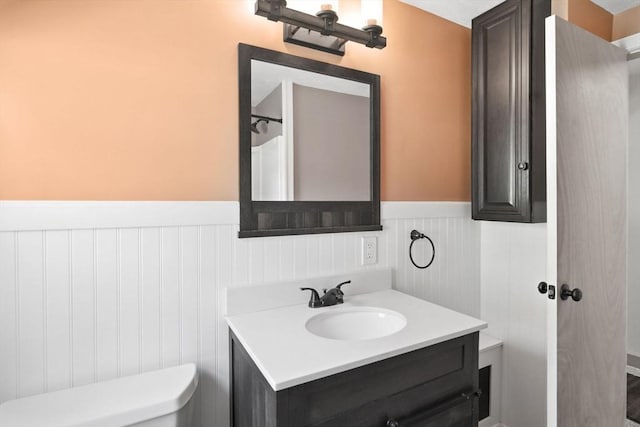 bathroom with a wainscoted wall, vanity, and toilet