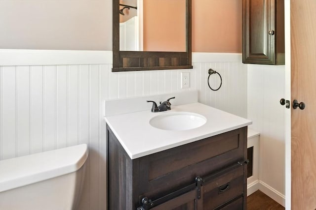 bathroom featuring vanity, a wainscoted wall, a decorative wall, and toilet
