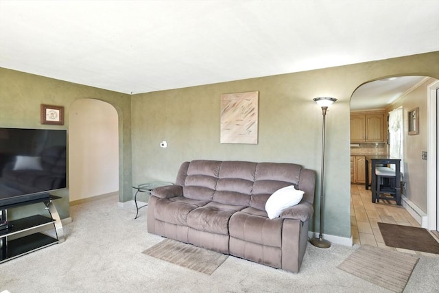 living room featuring light colored carpet, arched walkways, and baseboards