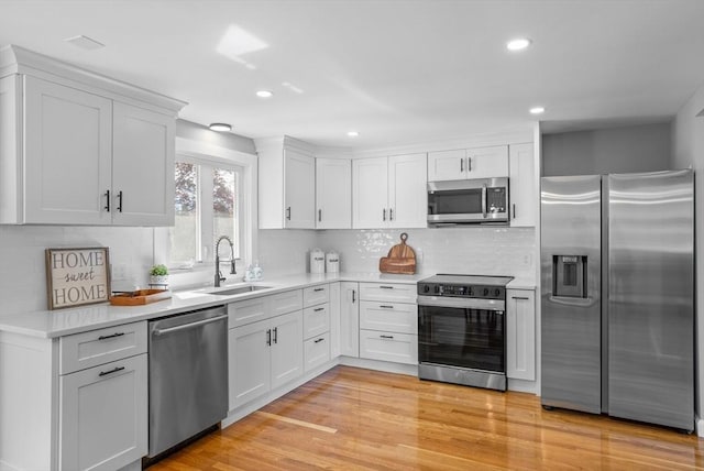 kitchen with decorative backsplash, appliances with stainless steel finishes, a sink, light countertops, and white cabinets