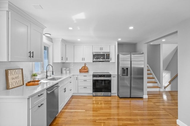 kitchen with backsplash, appliances with stainless steel finishes, a sink, and light wood-style flooring