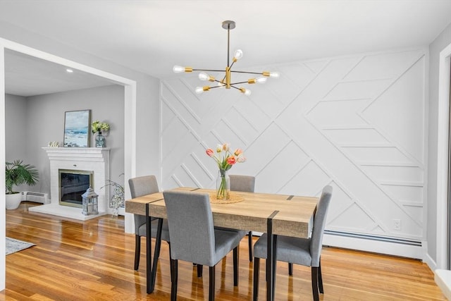 dining space with an inviting chandelier, a baseboard radiator, a decorative wall, and light wood finished floors