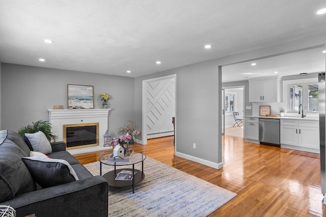 living room featuring light wood-style floors, a brick fireplace, recessed lighting, baseboards, and a baseboard radiator
