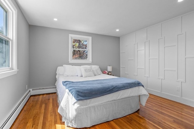 bedroom featuring recessed lighting, a baseboard heating unit, and wood finished floors