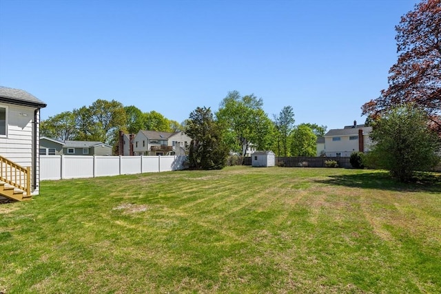 view of yard featuring a residential view, stairs, a storage shed, a fenced backyard, and an outbuilding