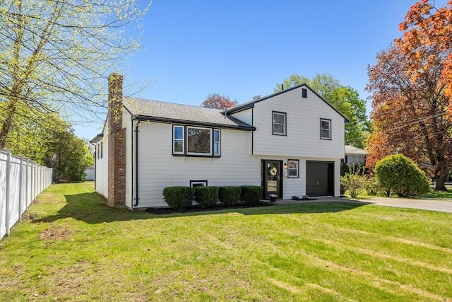 tri-level home featuring fence, a front yard, a chimney, concrete driveway, and an attached garage