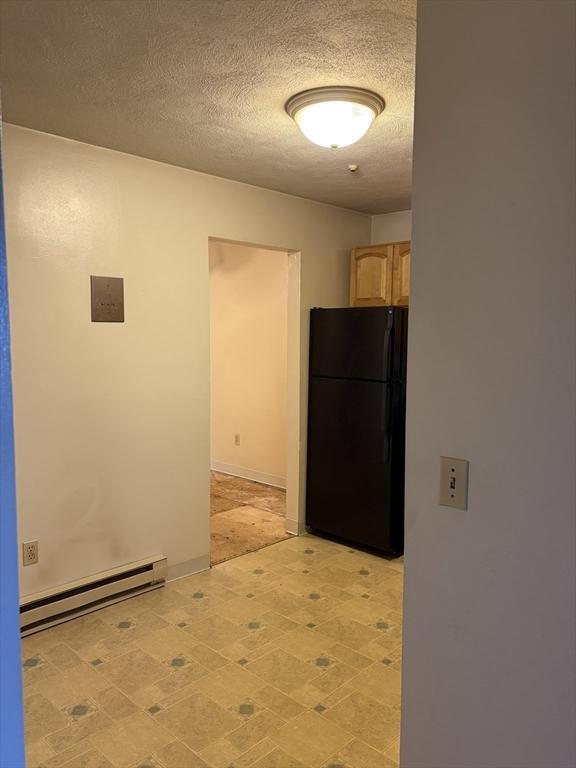 740 Central St Unit J11, Leominster, MA 01453 - kitchen featuring freestanding refrigerator, a baseboard heating unit, light brown cabinetry, a textured ceiling, and light floors