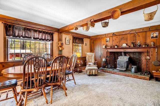 carpeted dining space with wooden walls, beamed ceiling, and a wood stove
