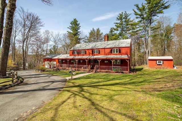 cabin with covered porch, a chimney, a front yard, an outdoor structure, and aphalt driveway