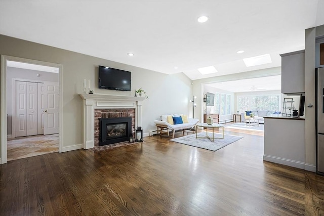 unfurnished living room featuring dark wood-type flooring, vaulted ceiling with skylight, and a brick fireplace