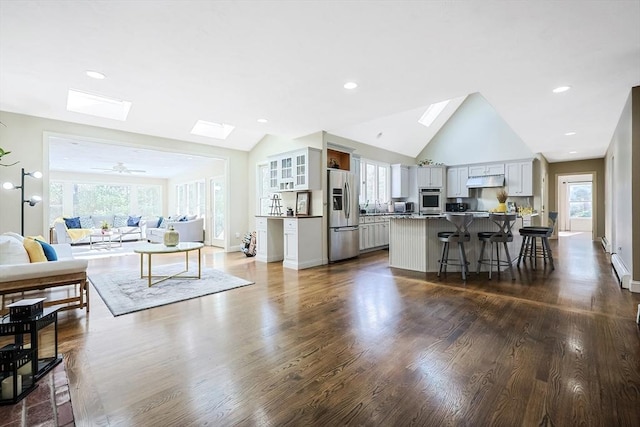 living room featuring ceiling fan, a baseboard heating unit, a skylight, high vaulted ceiling, and dark hardwood / wood-style floors