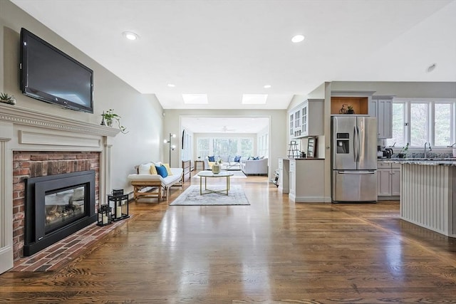 living room featuring a brick fireplace, sink, dark hardwood / wood-style flooring, and a skylight