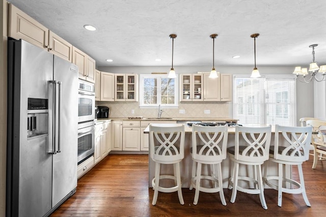 kitchen featuring dark wood-style flooring, stainless steel appliances, light countertops, glass insert cabinets, and a sink