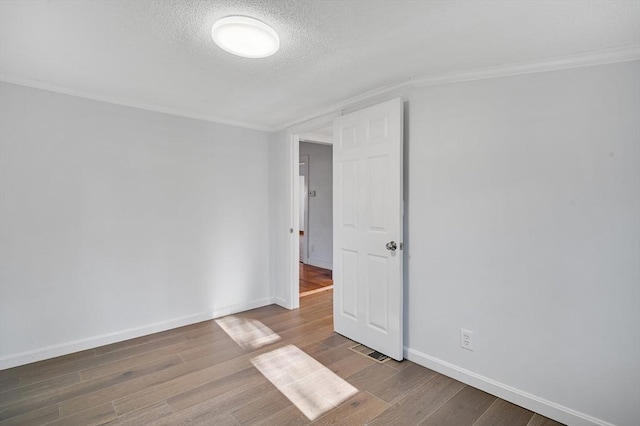 empty room with hardwood / wood-style flooring, ornamental molding, and a textured ceiling