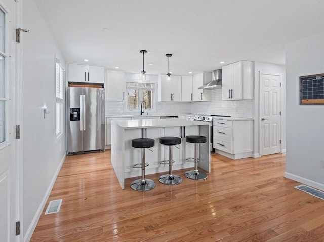 kitchen featuring visible vents, a breakfast bar area, wall chimney range hood, a center island, and appliances with stainless steel finishes