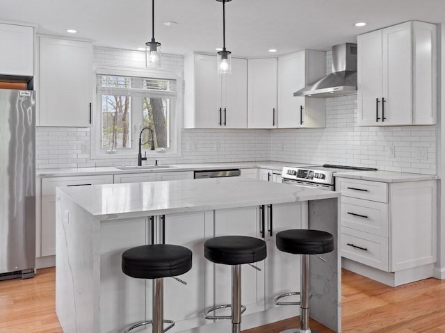 kitchen featuring a kitchen breakfast bar, wall chimney range hood, white cabinetry, a sink, and stainless steel appliances