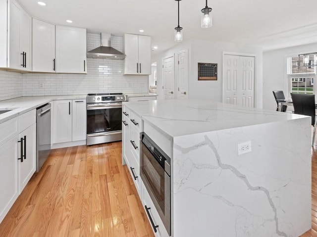 kitchen featuring wall chimney range hood, white cabinets, light wood finished floors, stainless steel appliances, and tasteful backsplash