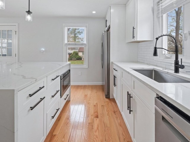 kitchen with appliances with stainless steel finishes, hanging light fixtures, white cabinetry, a sink, and light wood-style flooring