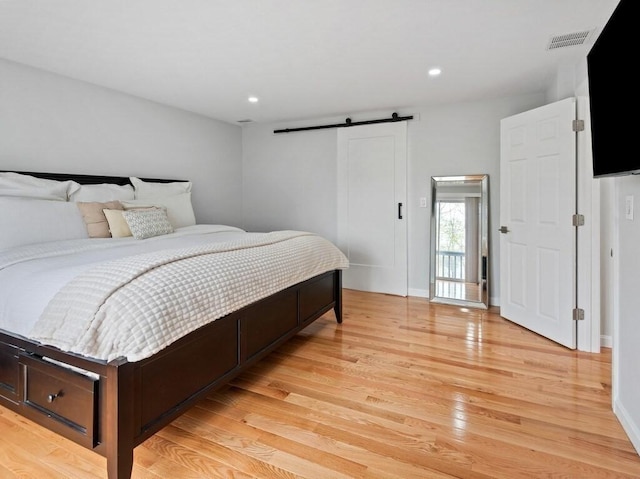 bedroom featuring visible vents, a barn door, light wood-style flooring, and recessed lighting