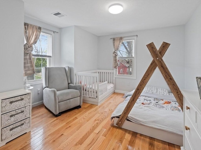 bedroom featuring baseboards, multiple windows, wood finished floors, and visible vents