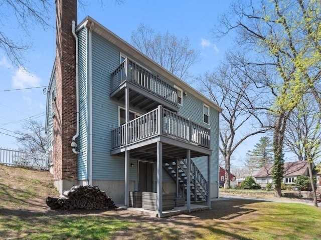 back of house featuring fence, a balcony, a deck, a chimney, and stairway