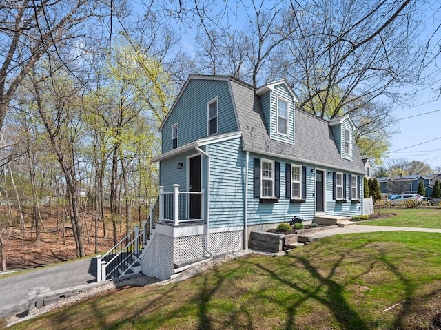 dutch colonial featuring a gambrel roof, a front lawn, and a shingled roof