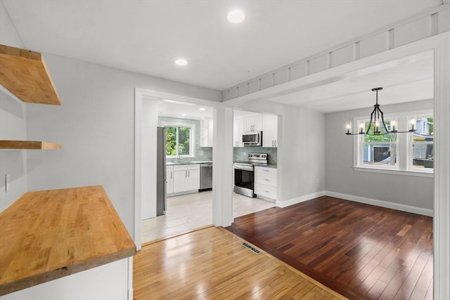 67 Great Neck Rd, Wareham, MA 02571 - kitchen featuring stainless steel appliances, light wood finished floors, a chandelier, a sink, and white cabinetry