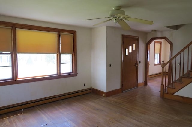 foyer featuring a baseboard heating unit, baseboards, wood finished floors, a ceiling fan, and stairway