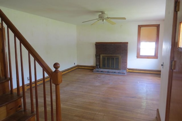 unfurnished living room with a ceiling fan, baseboard heating, wood finished floors, a brick fireplace, and baseboards