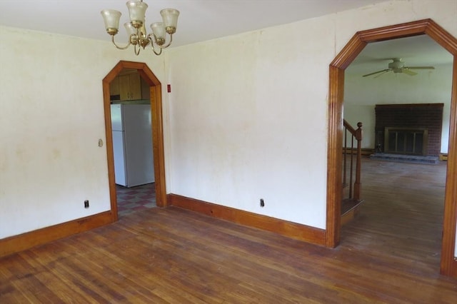 unfurnished room featuring baseboards, ceiling fan, wood finished floors, arched walkways, and a chandelier
