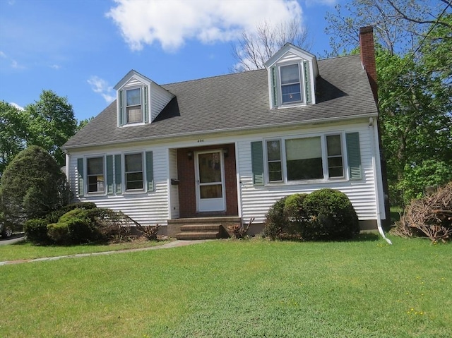 new england style home with a chimney, a front yard, entry steps, and a shingled roof