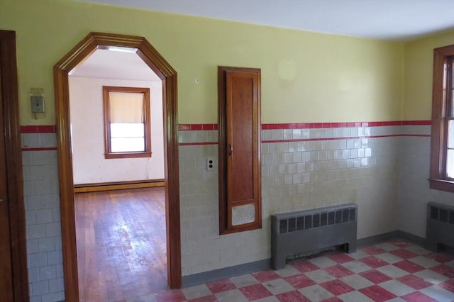 empty room with radiator heating unit, tile walls, tile patterned floors, a wainscoted wall, and a baseboard heating unit