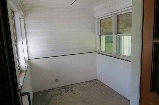 empty room featuring unfinished concrete floors, plenty of natural light, and wooden walls