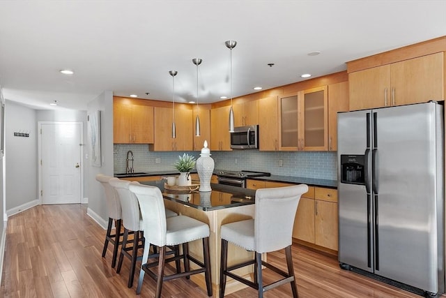 kitchen featuring appliances with stainless steel finishes, tasteful backsplash, sink, hanging light fixtures, and light wood-type flooring