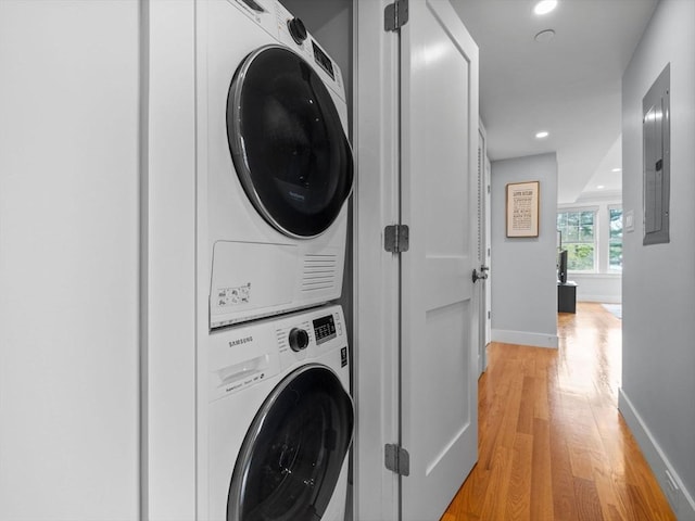 laundry room featuring baseboards, laundry area, light wood finished floors, and stacked washer / dryer