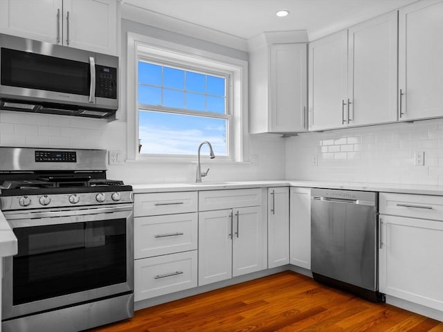 kitchen with appliances with stainless steel finishes, tasteful backsplash, light countertops, a sink, and white cabinetry