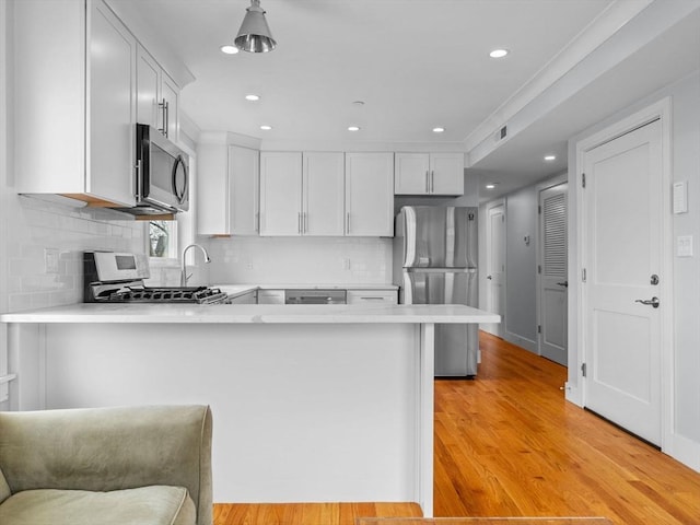 kitchen with a peninsula, light countertops, white cabinets, light wood-style flooring, and stainless steel appliances