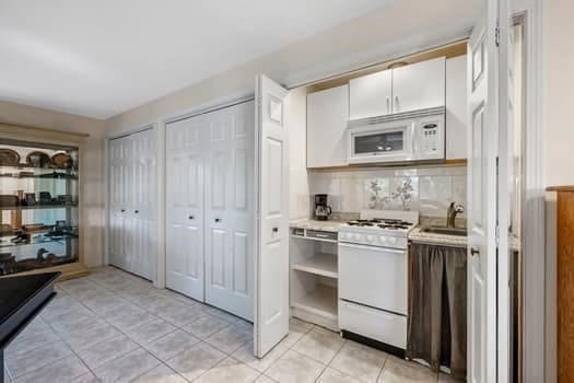 kitchen featuring light tile patterned flooring, sink, tasteful backsplash, white appliances, and white cabinetry