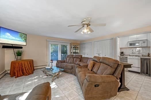 living room featuring ceiling fan, light tile patterned flooring, and a baseboard heating unit