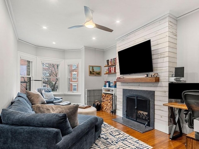 living room with a large fireplace, hardwood / wood-style flooring, ceiling fan, and ornamental molding