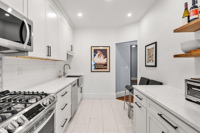 kitchen with light stone countertops, white cabinetry, sink, stainless steel appliances, and backsplash