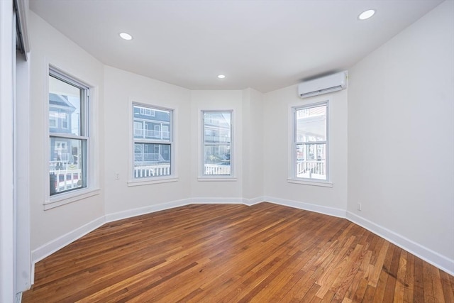 unfurnished room with baseboards, an AC wall unit, and hardwood / wood-style flooring